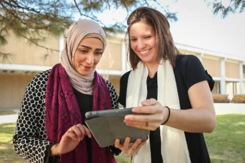 两位女性演讲者在米切纳图书馆外一起看iPad.